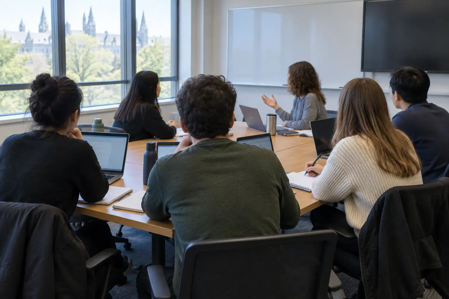 A postgraduate seminar group around a table with laptops and notebooks seen from behind